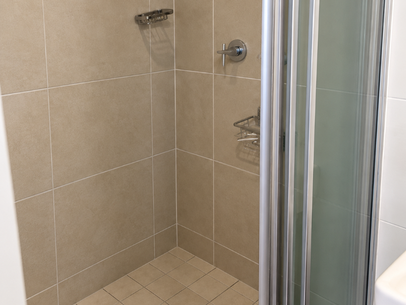A clean, modern shower enclosure featuring neutral wall tiles, a glass folding screen, and integrated chrome fixtures.