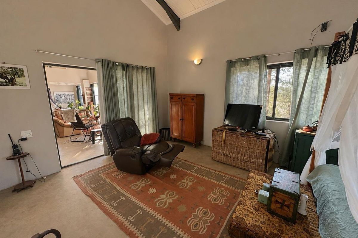 A living room featuring a high vaulted ceiling with an exposed beam, neutral walls, and a large sliding glass door leading to an adjacent space.