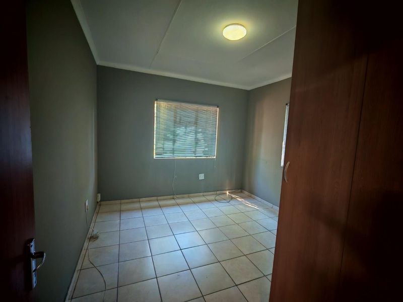 An empty bedroom featuring tiled flooring, built-in cupboards, and venetian blinds, offering a neutral canvas for personalization.