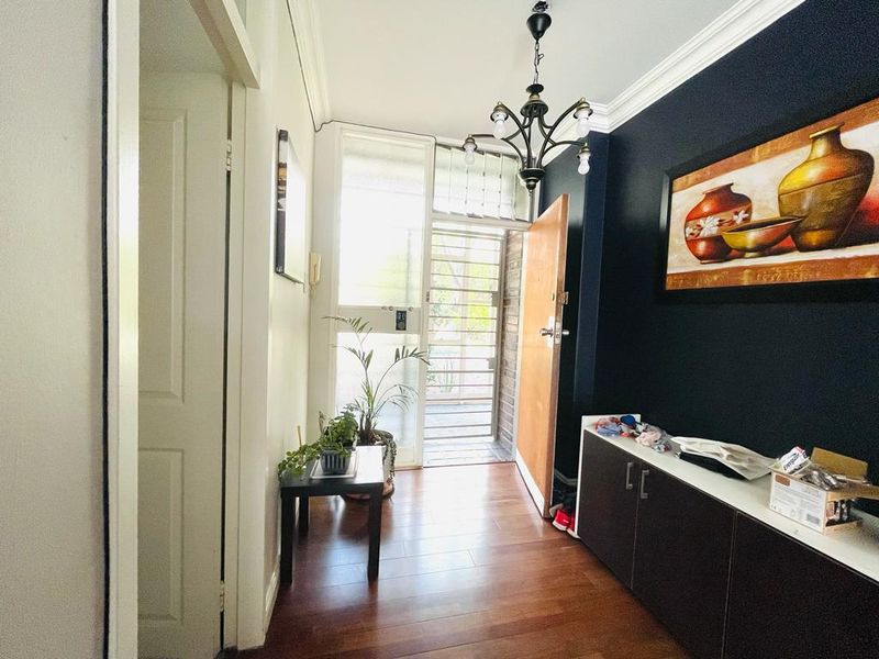 A welcoming apartment entrance featuring laminate flooring, crown molding, and a decorative chandelier, leading to a secure exterior gate.