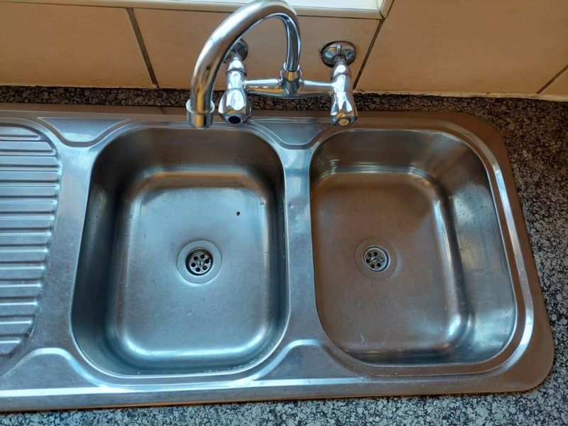A functional stainless steel double bowl kitchen sink with a chrome mixer tap set into a granite countertop with tiled splashback.