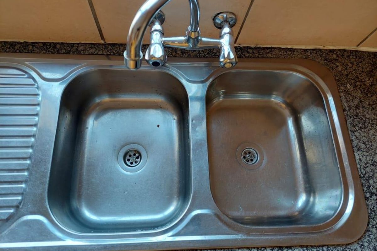 A functional stainless steel double bowl kitchen sink with a chrome mixer tap set into a granite countertop with tiled splashback.