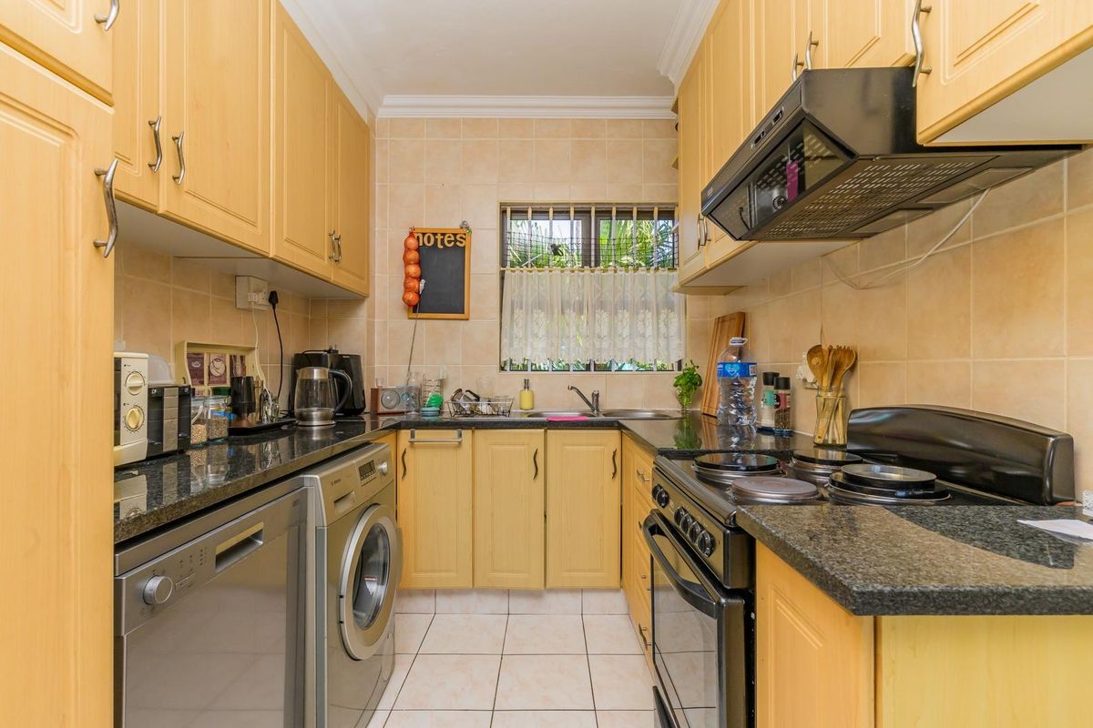 A functional galley-style kitchen featuring light wood cabinetry, granite countertops, tiled splashbacks, and integrated space for laundry appliances.