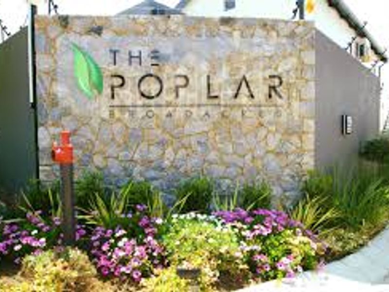 The entrance signage and stone feature wall of The Poplar complex, featuring manicured garden beds and integrated security fencing.