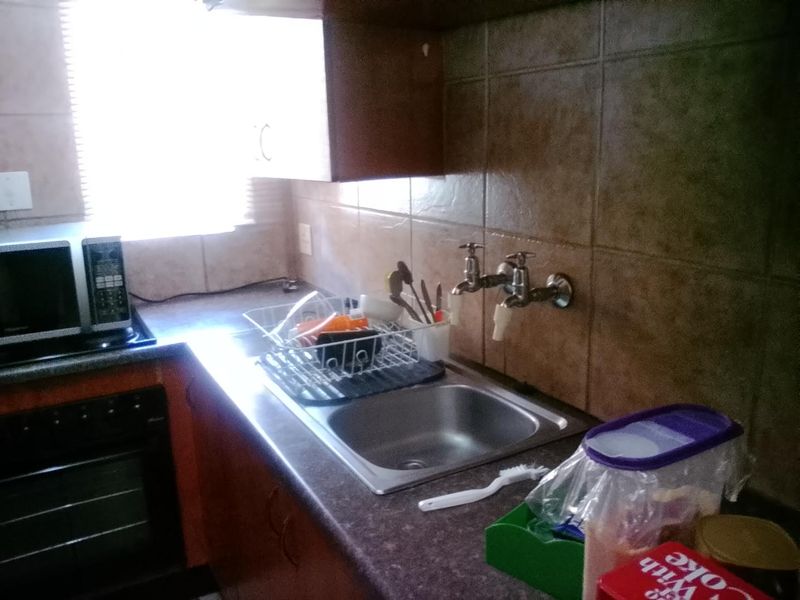A compact kitchen area featuring a stainless steel sink, wall-mounted taps, built-in oven, and tiled backsplash with overhead cabinetry.