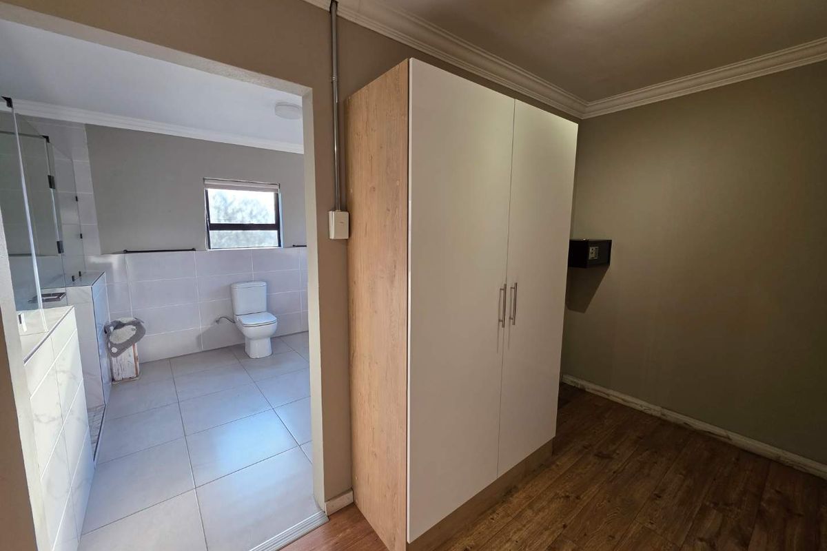 A bedroom featuring wood-look flooring and a built-in wardrobe, with an adjoining en-suite bathroom equipped with tiled finishes and a toilet.
