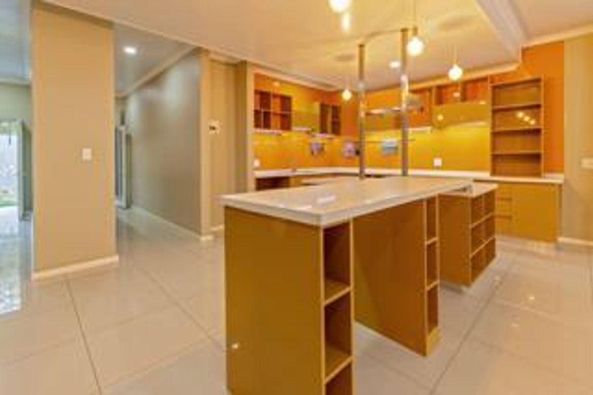 Modern open-plan kitchen featuring built-in cabinetry, a central breakfast island with stone countertop, and tiled flooring throughout.