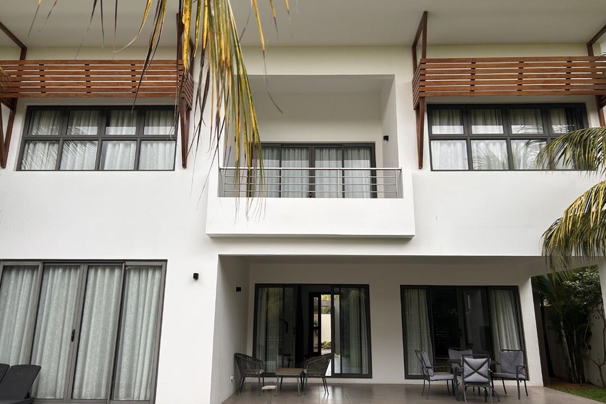 Rear elevation of a modern two-story house featuring a ground floor patio, upper-level balcony, and large sliding glass doors with dark frames.