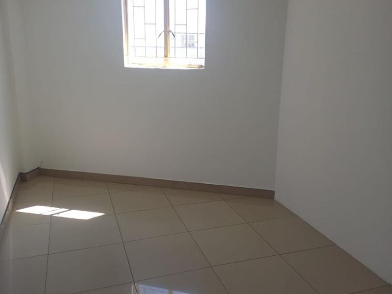 A clean, empty office space featuring neutral tiled flooring, recessed ceiling lighting, and a window fitted with security bars.