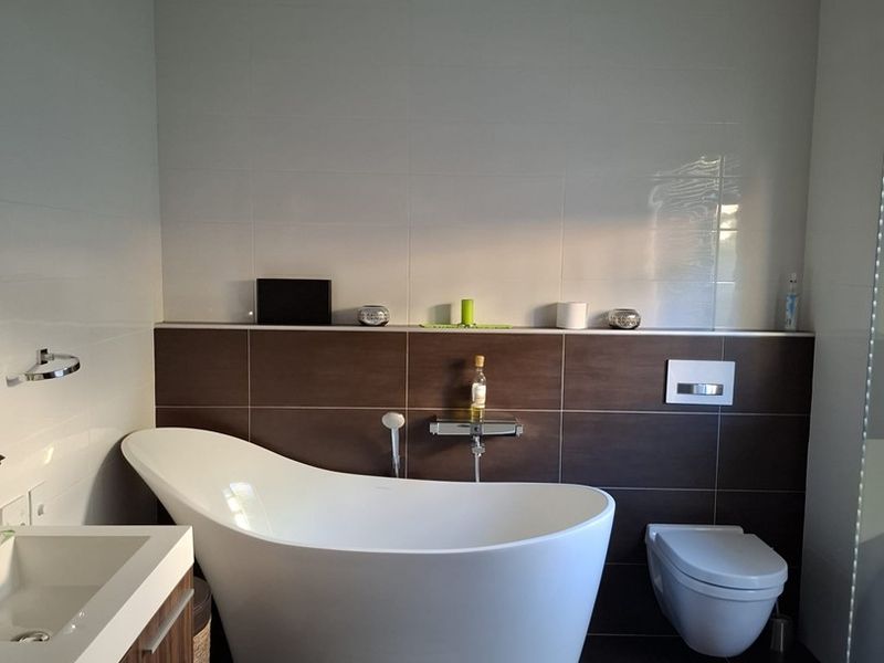 Modern bathroom featuring a sleek freestanding bathtub, wall-mounted toilet, and a contemporary vanity unit with integrated basin, finished with high-quality floor and wall tiling.