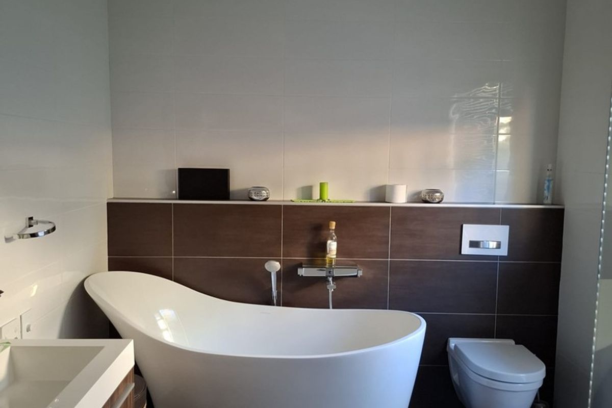 Modern bathroom featuring a sleek freestanding bathtub, wall-mounted toilet, and a contemporary vanity unit with integrated basin, finished with high-quality floor and wall tiling.