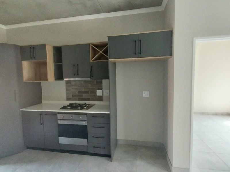 Modern kitchen featuring dark grey cabinetry, stone countertops, built-in gas hob, electric oven, and an industrial-style exposed concrete ceiling.