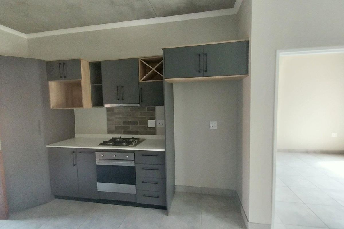 Modern kitchen featuring dark grey cabinetry, stone countertops, built-in gas hob, electric oven, and an industrial-style exposed concrete ceiling.