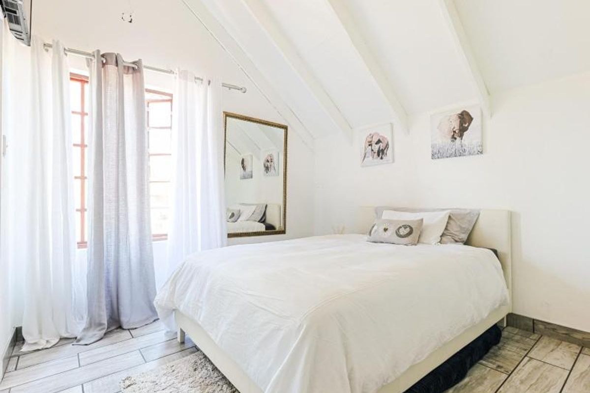 A bright bedroom featuring exposed white rafters, tiled flooring, and large windows allowing for ample natural light.