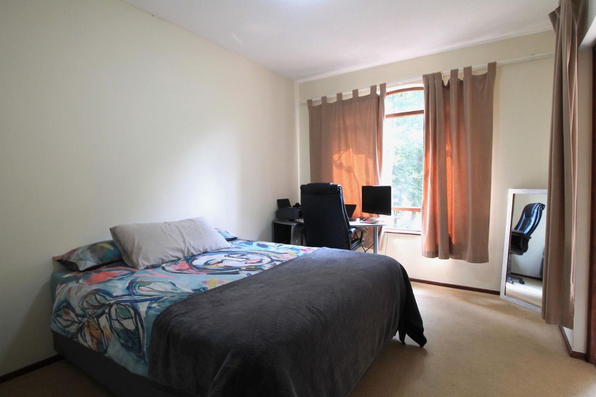 A bedroom featuring carpeted flooring and a large window with curtains, providing natural light and a view of the outdoors.