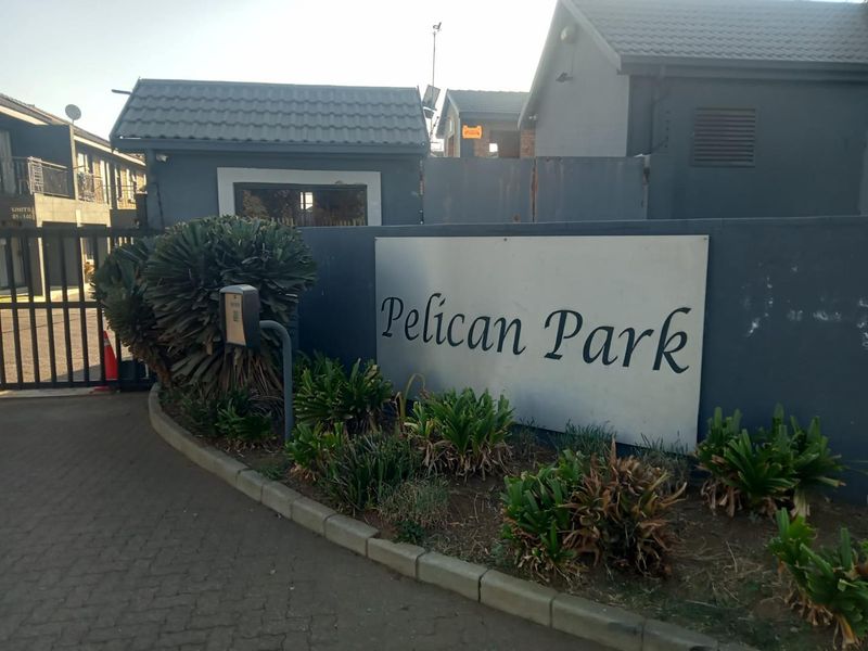 Entrance view of Pelican Park townhouse complex featuring a security gate, paved driveway, and complex signage.