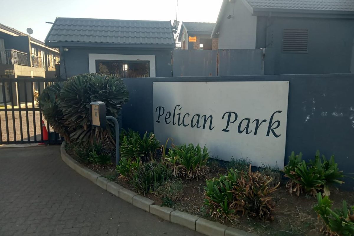 Entrance view of Pelican Park townhouse complex featuring a security gate, paved driveway, and complex signage.