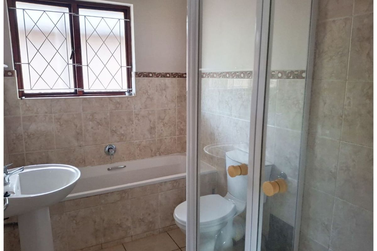 A functional bathroom featuring a pedestal basin, a built-in bathtub, and a separate glass-enclosed shower with neutral wall and floor tiling.