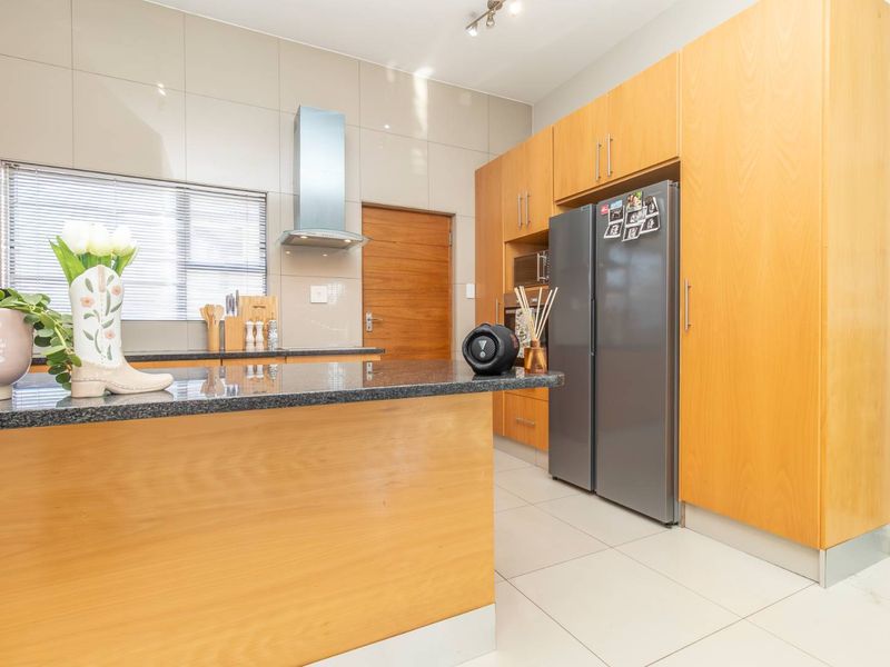 A well-maintained kitchen featuring light wood cabinetry, granite countertops, a stainless steel extractor fan, and neutral tiled flooring.