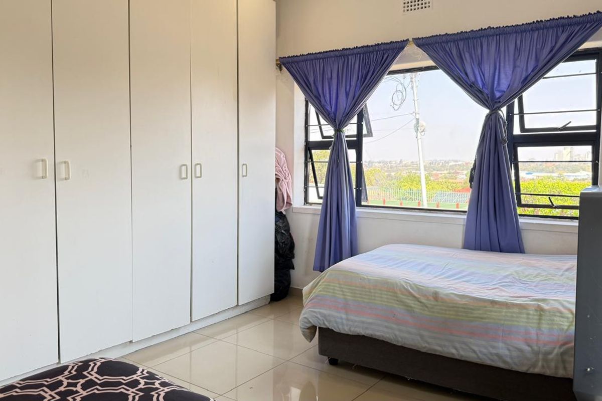 A bedroom featuring built-in floor-to-ceiling wardrobes, tiled flooring, and large windows providing natural light and an elevated view.