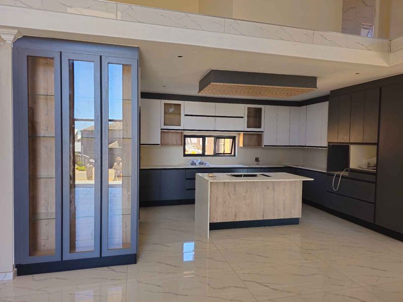 Modern kitchen featuring two-tone cabinetry, a central island with stone countertop, integrated display shelving, and high-gloss tiled flooring.