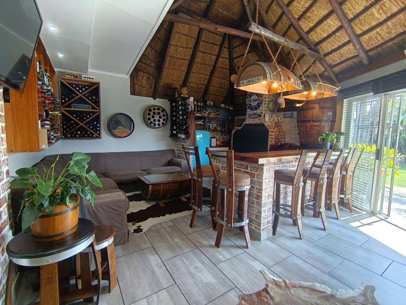 A rustic-style entertainment bar area featuring a thatched roof, brick bar counter, built-in wine storage, and large sliding doors opening to the garden.