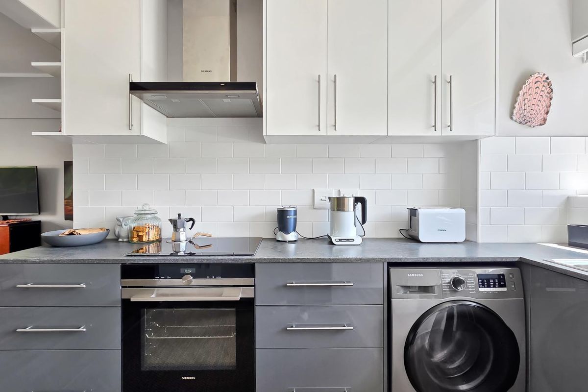 Modern kitchen featuring high-gloss cabinetry, subway tile backsplash, integrated oven, induction hob, extractor fan, and a built-in washing machine.
