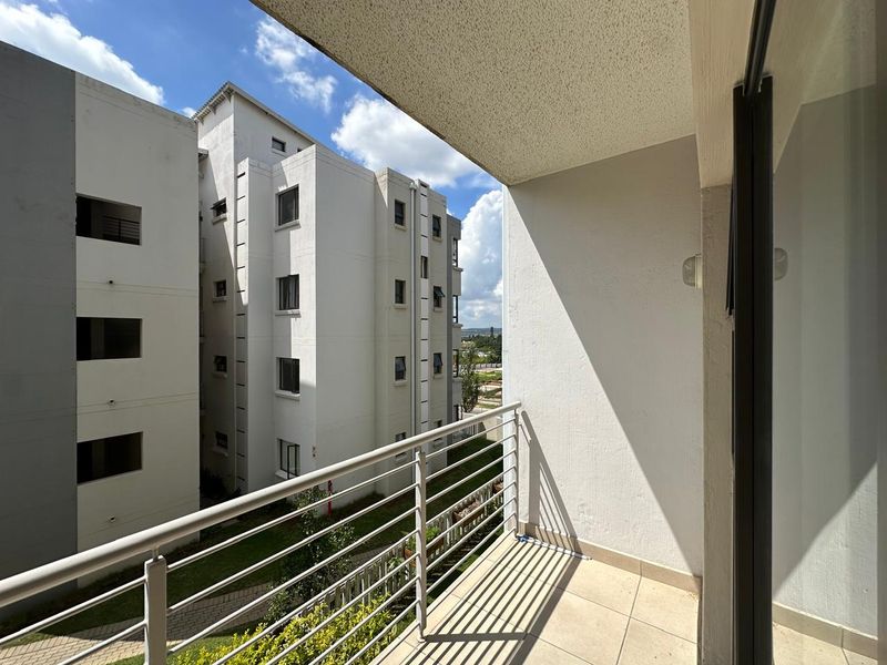 A clean, modern balcony with tiled flooring and a metal balustrade, offering an open view of the surrounding apartment complex.