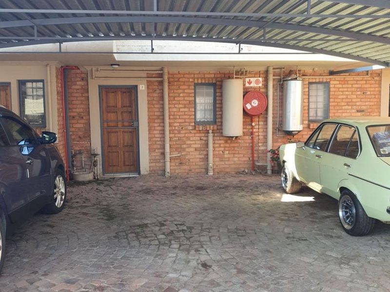 A covered carport area featuring brick facade walls, cobblestone paving, and integrated utility fixtures including a fire hose reel and water heater.