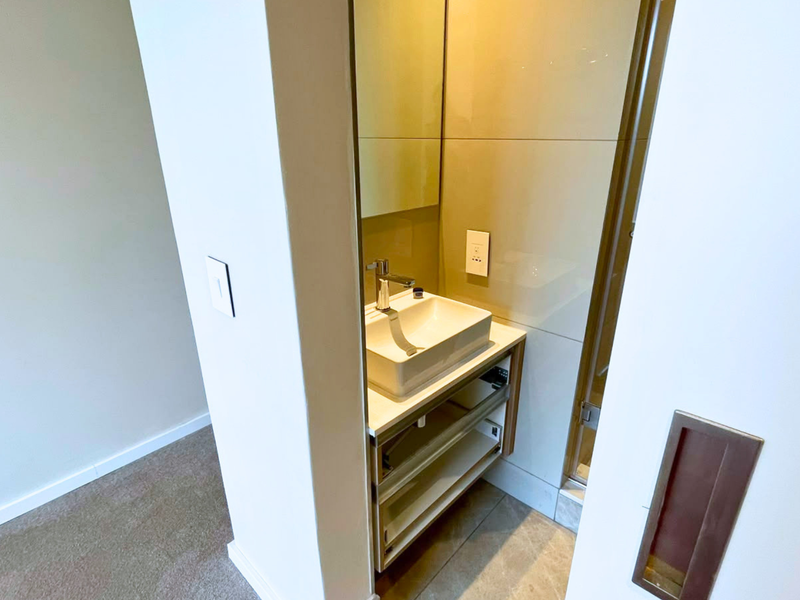 A compact, modern bathroom vanity area featuring a vessel sink, chrome faucet, and wall-mounted mirror with tiled splashback.