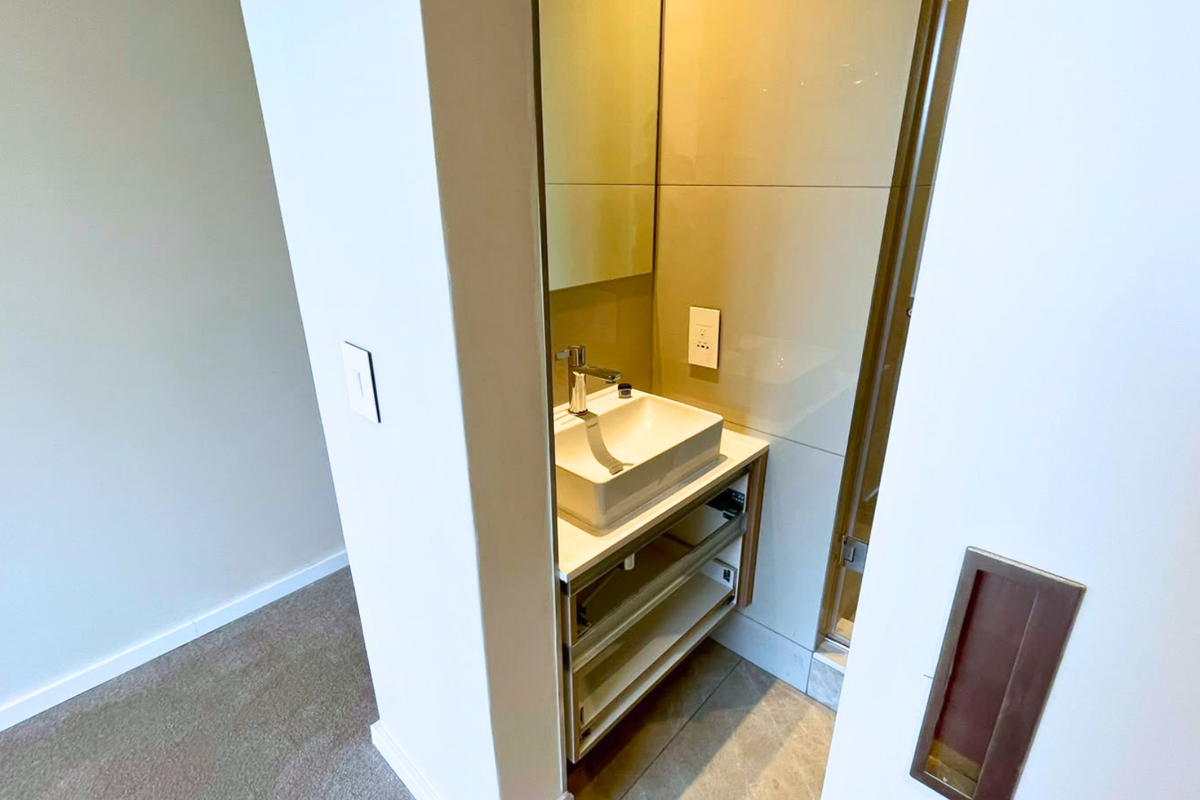 A compact, modern bathroom vanity area featuring a vessel sink, chrome faucet, and wall-mounted mirror with tiled splashback.