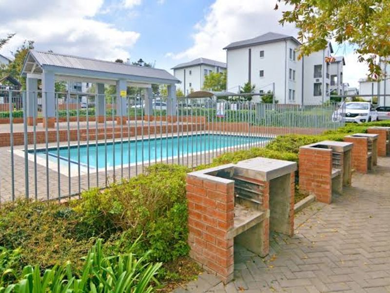 Communal outdoor pool area featuring a covered pavilion, paved patio space, and multiple built-in brick braai stands for resident use.