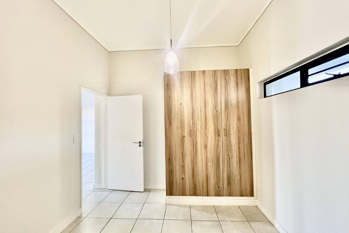 A bright, empty bedroom featuring neutral tiled flooring, modern wood-finish built-in cupboards, and a high-level clerestory window for natural light.