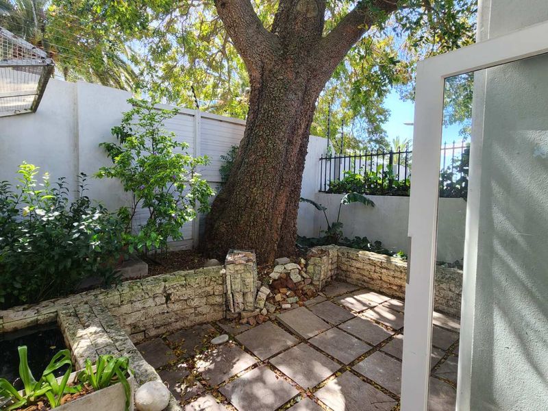 Private garden area featuring a paved patio, mature tree, and stone retaining wall with a small water feature.