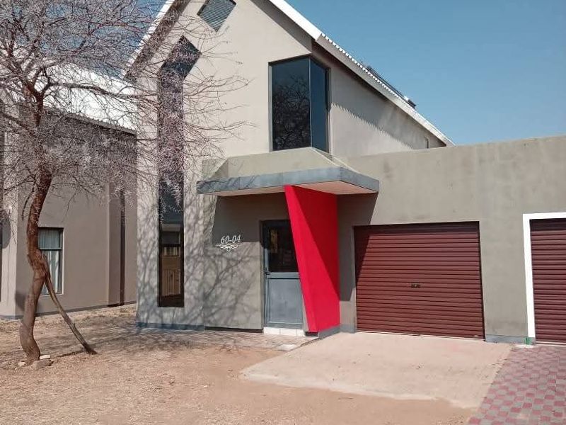 Front elevation of a modern townhouse featuring a pitched roof, roller garage door, and a distinctive red accent pillar at the entrance.
