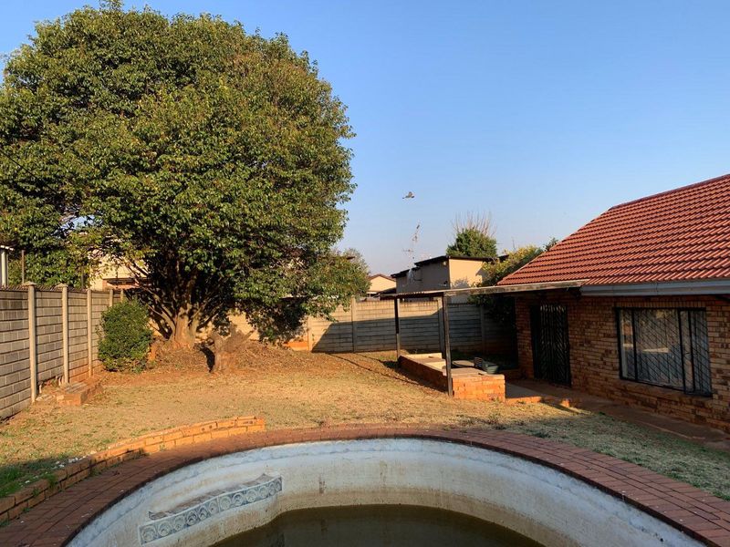 Rear garden area featuring a swimming pool, brick boundary walls, and a covered patio attached to the main brick residence.