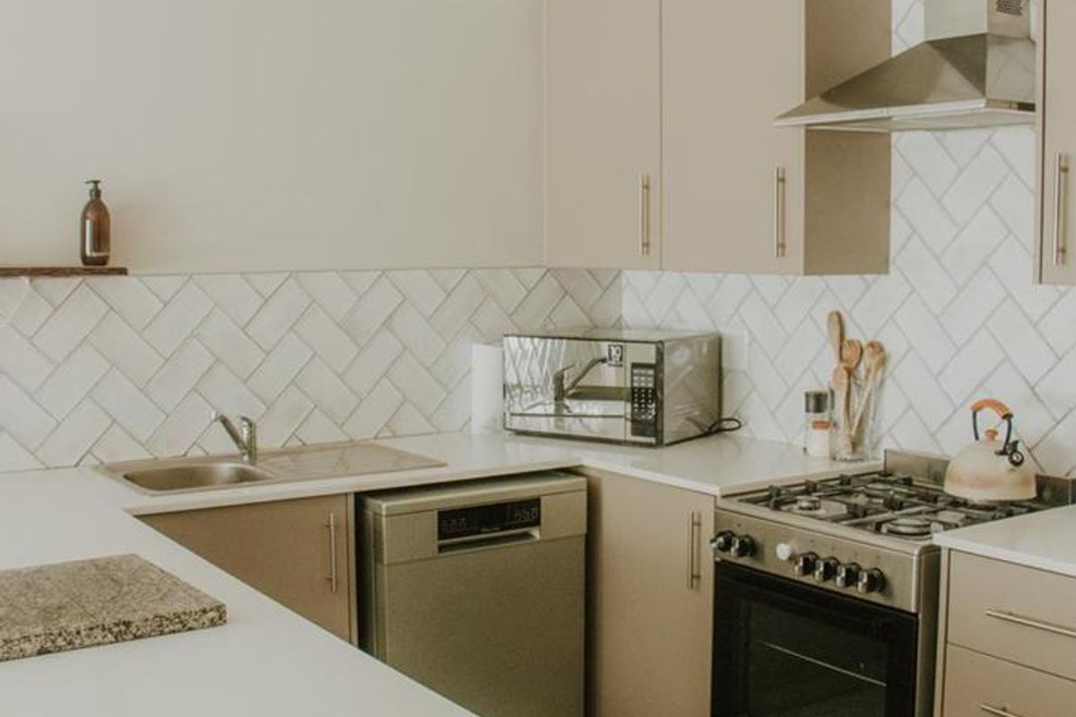 Modern kitchen featuring neutral cabinetry, herringbone tile backsplash, stainless steel appliances, and clean quartz countertops in a functional layout.