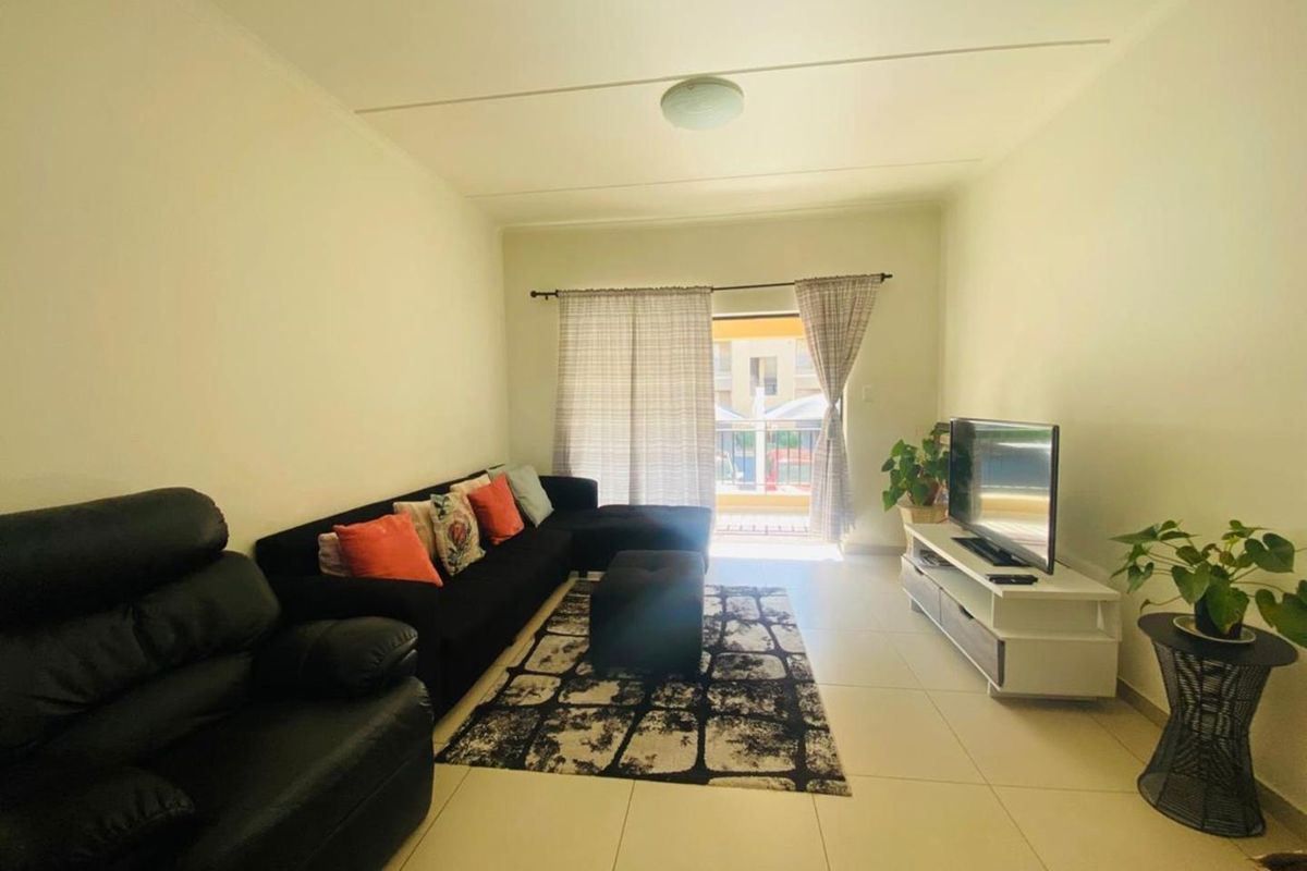 A bright living room featuring neutral floor tiles and a sliding door leading to an outdoor balcony area.