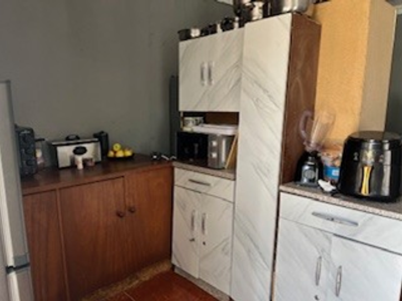A compact kitchen area featuring a mix of dark wood and marble-effect cabinetry with tiled flooring, requiring cosmetic updates to improve aesthetic cohesion.