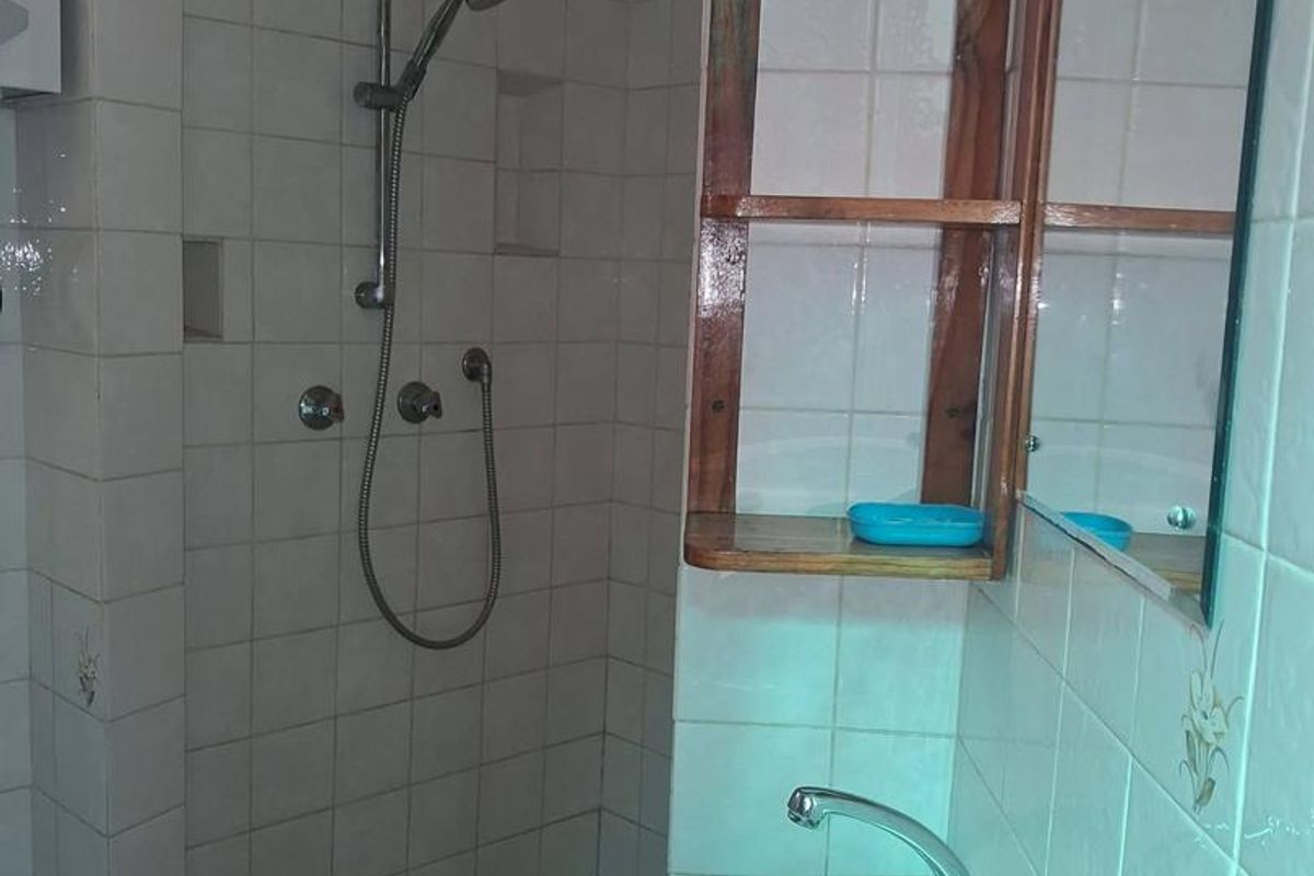 A functional bathroom featuring a tiled shower enclosure, pedestal basin, and built-in wooden shelving with a wall mirror.