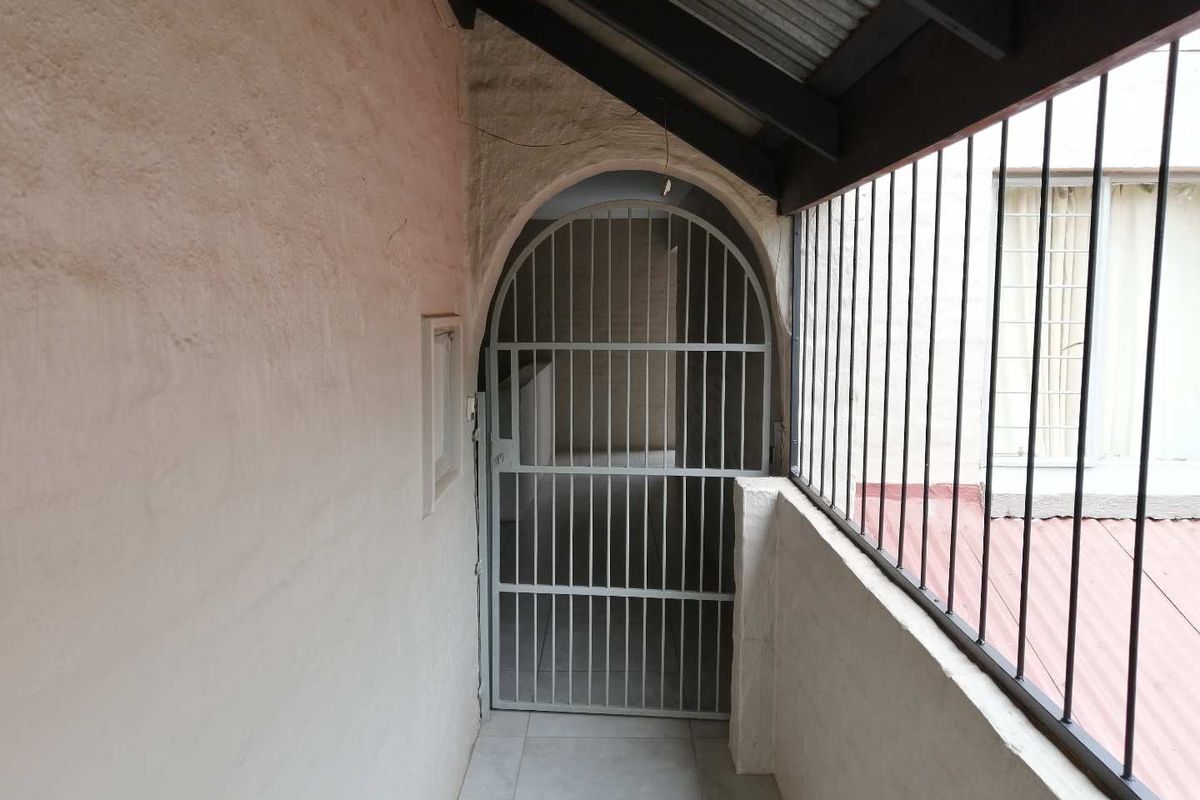 A covered balcony area featuring a security gate, metal balustrade, and tiled flooring, showing signs of wear on the wall finish.