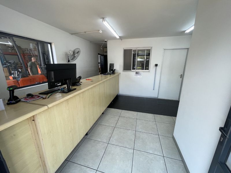 Functional industrial office space featuring a built-in reception counter, tiled flooring, and a service window overlooking the warehouse area.
