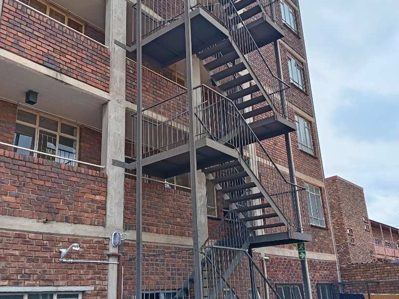 Exterior view of an apartment building featuring a multi-level steel fire escape staircase and traditional face brick facade.