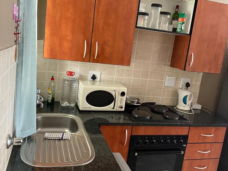 Compact kitchen featuring laminate cabinetry, granite countertops, a stainless steel sink, and a built-in oven with an electric hob.