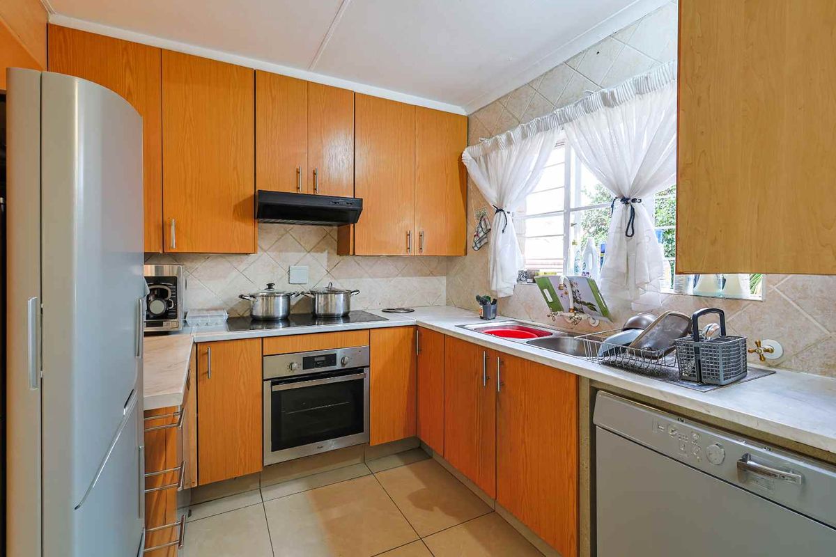 A functional kitchen featuring wood-finish cabinetry, tiled splashbacks, a built-in oven, hob, extractor fan, and a double-basin sink.