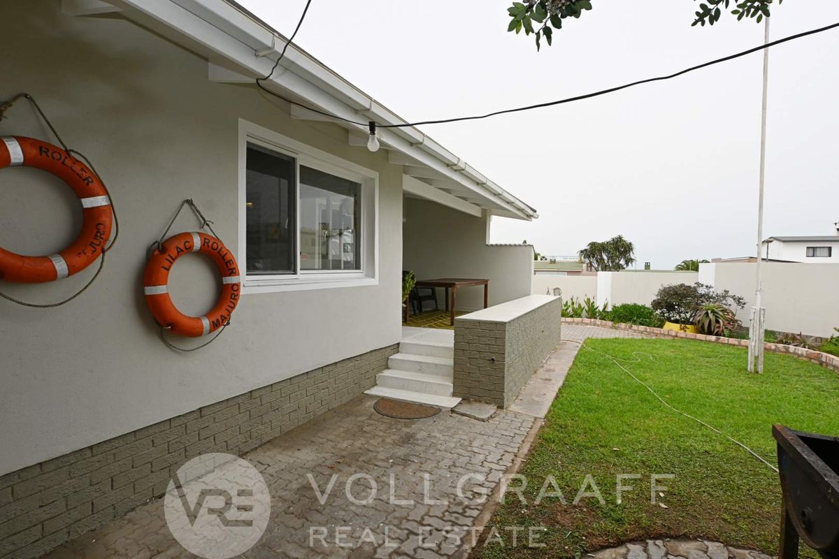 A rear exterior view featuring a covered patio area, paved walkway, and a small lawn with perimeter walling.