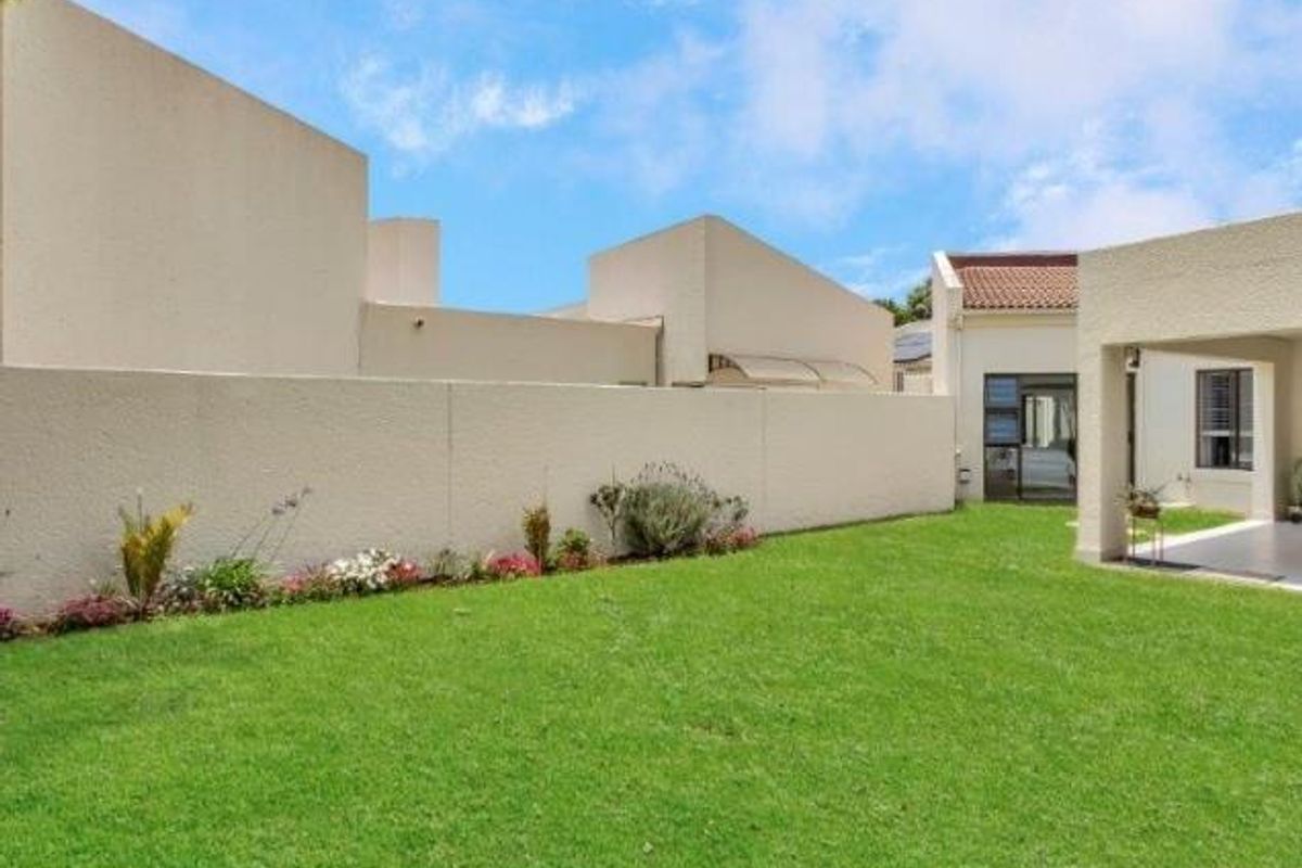 A well-maintained private garden area featuring a lush green lawn, perimeter boundary walls, and a covered patio space.