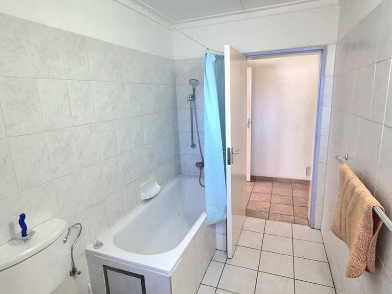 A functional bathroom featuring a bathtub with shower attachment, toilet, and tiled finishes. The space is dated and would benefit from modern updates.