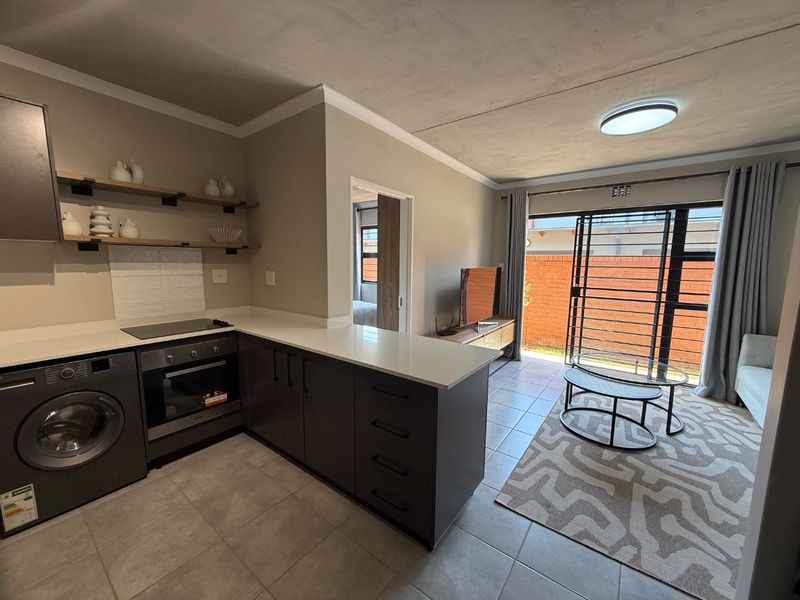 Modern open-plan kitchen and living area featuring sleek cabinetry, stone countertops, integrated appliances, and direct access to a private outdoor space.