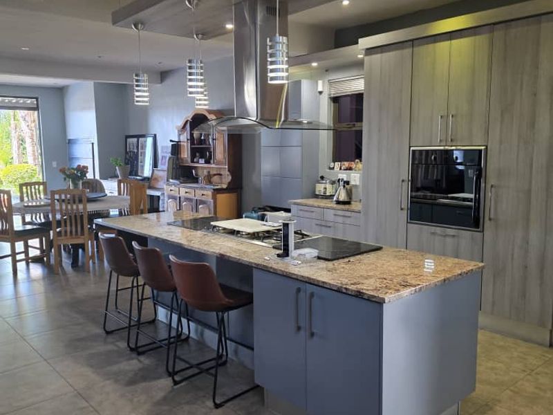 Modern open-plan kitchen featuring a large island with stone countertops, built-in appliances, and a distinctive suspended ceiling feature with integrated lighting.